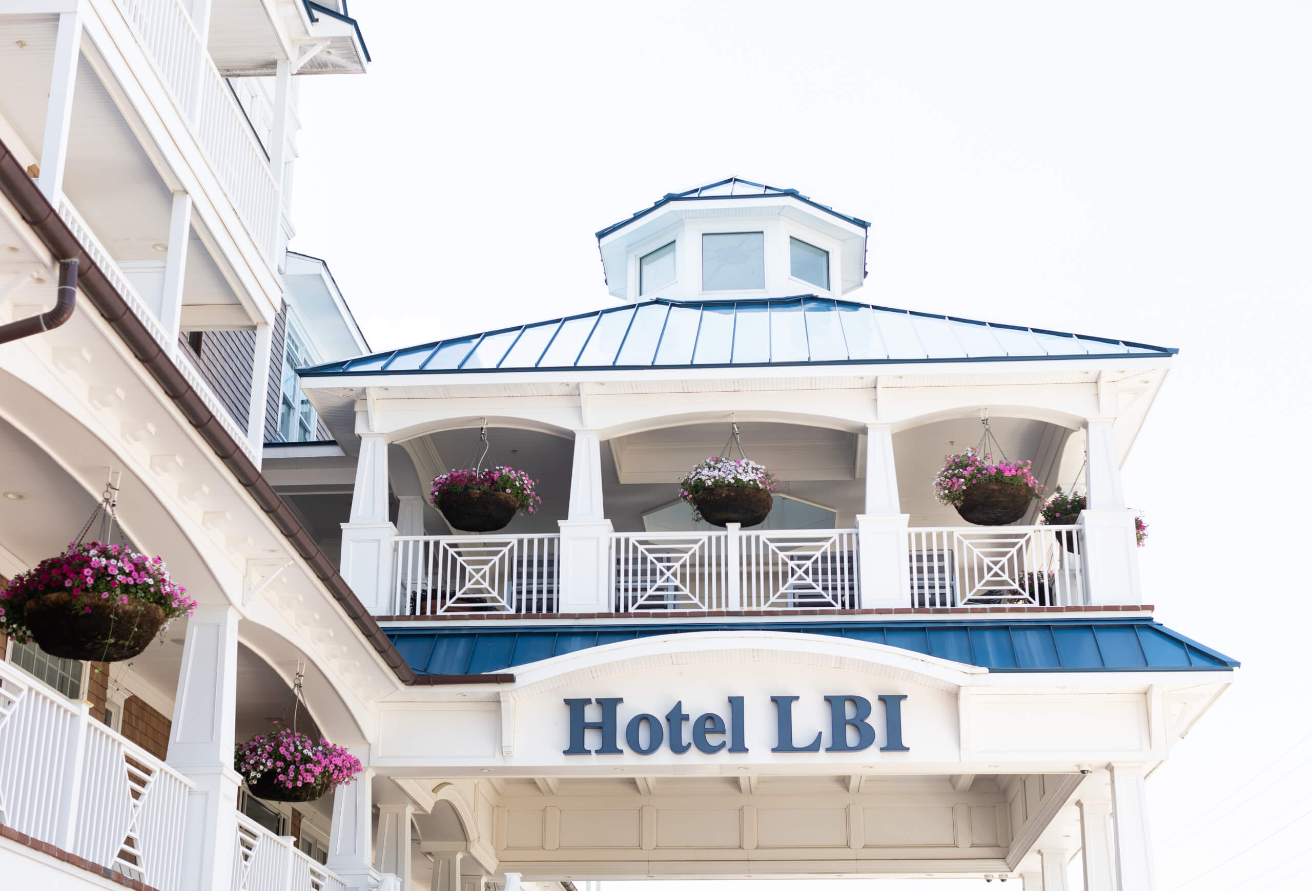 The exterior of Hotel LBI, showing its white facade, blue roof, and hanging flower baskets.